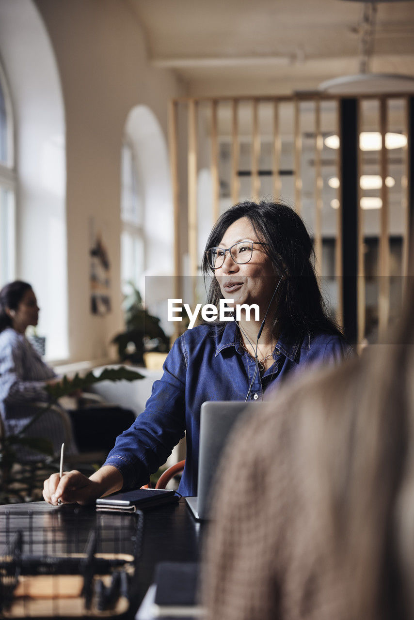 Smiling female business professional talking through wired headphones at coworking office