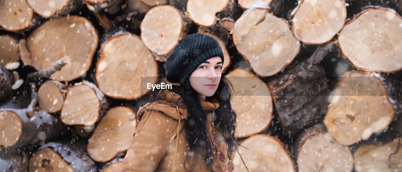 Portrait of young woman standing against firewood