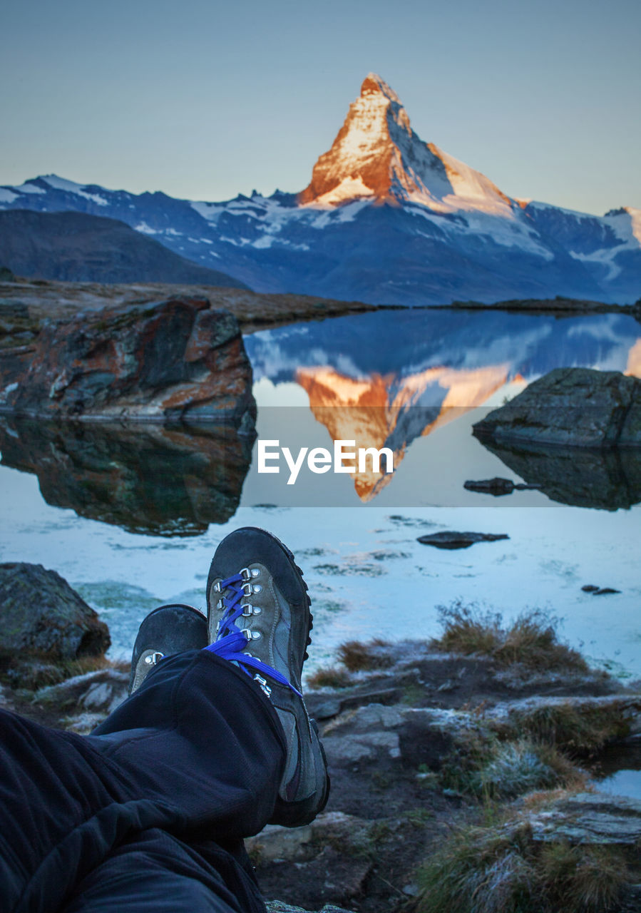 Low section of man with reflection in lake against sky