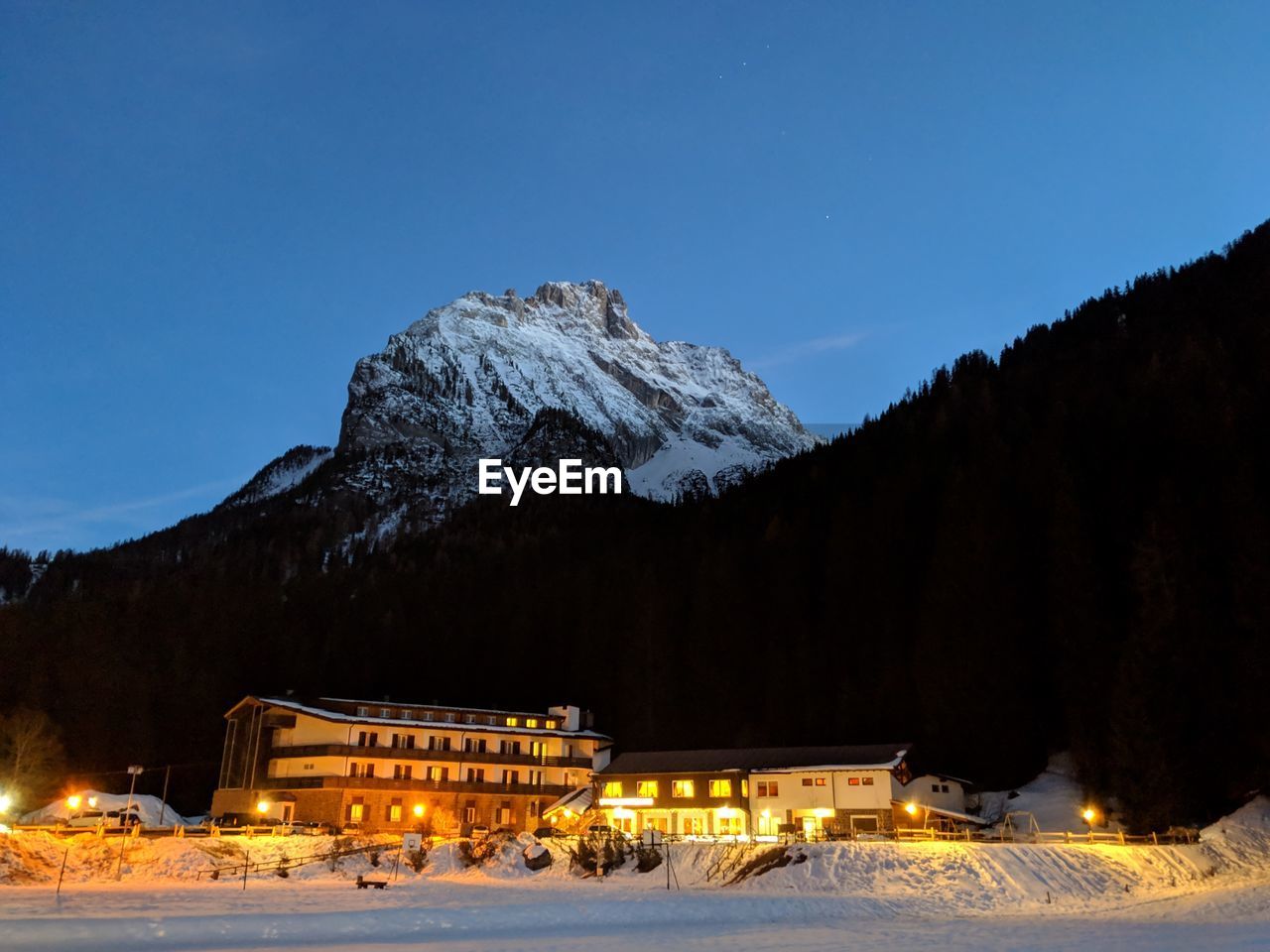Illuminated building against snowcapped mountains at night