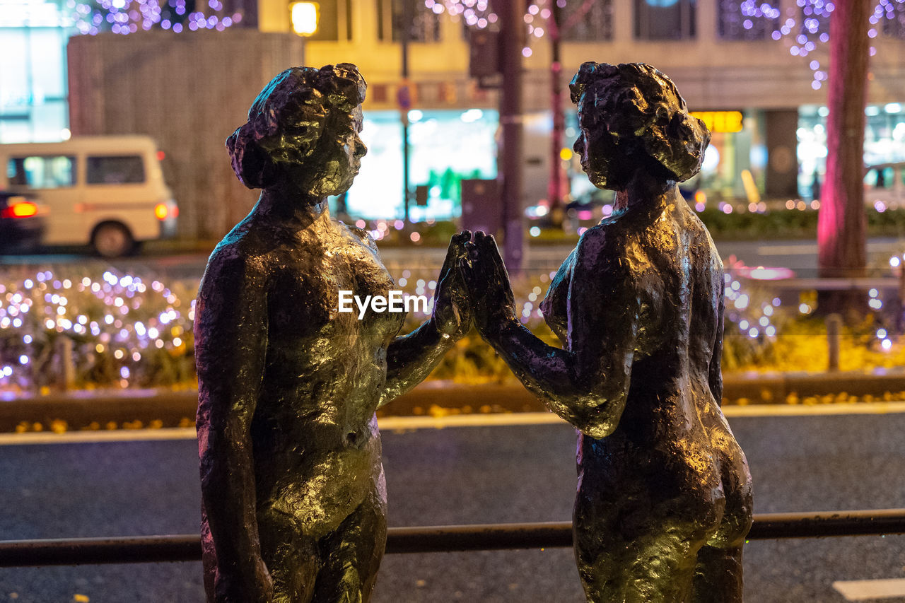 STATUE AGAINST ILLUMINATED CITY