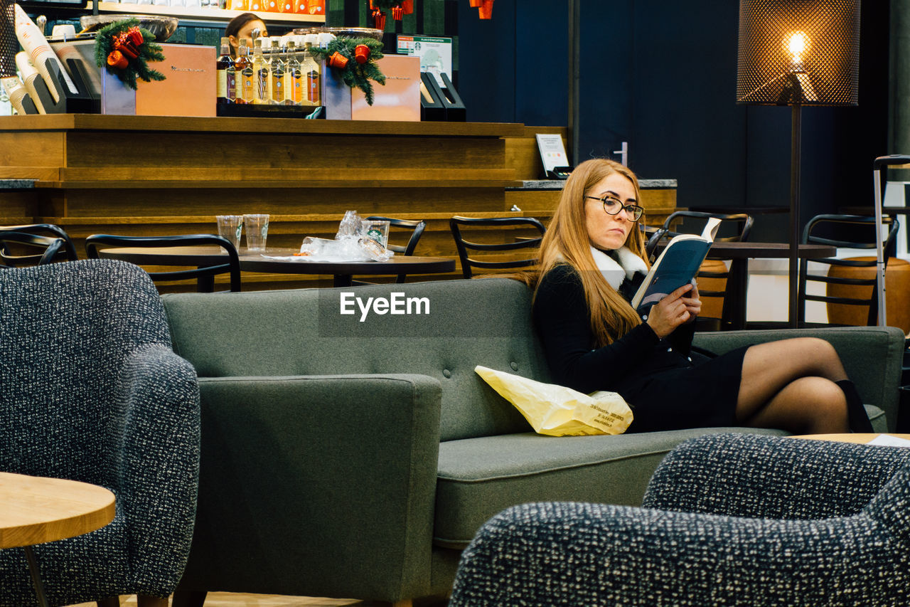 WOMAN USING MOBILE PHONE WHILE SITTING IN SOFA