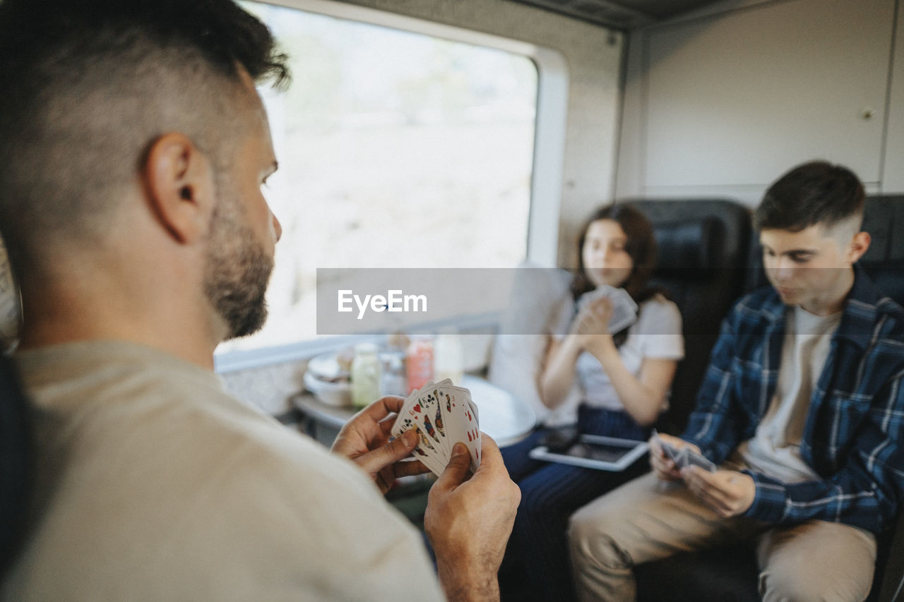 Father playing cards with son and daughter sitting in train