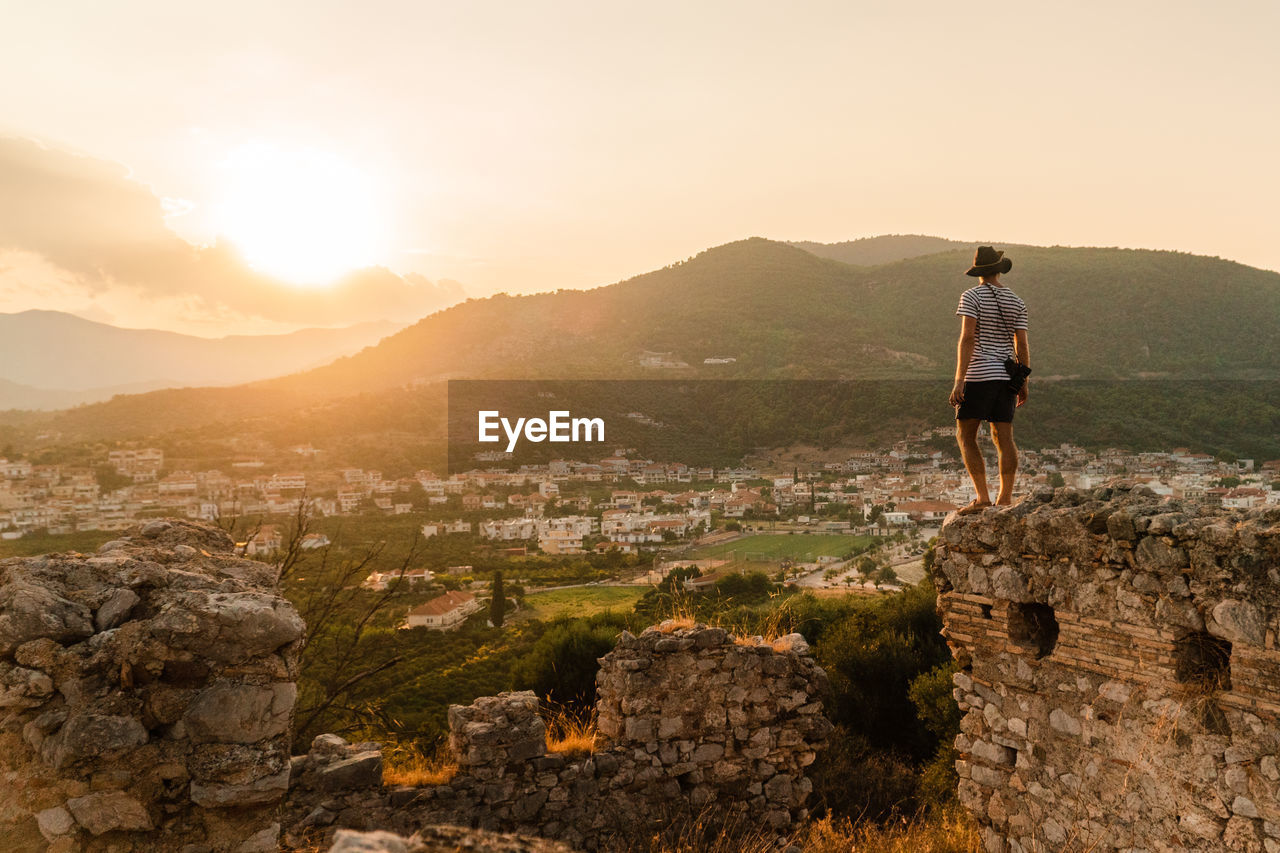 Rear view of man looking at landscape against sky during sunset