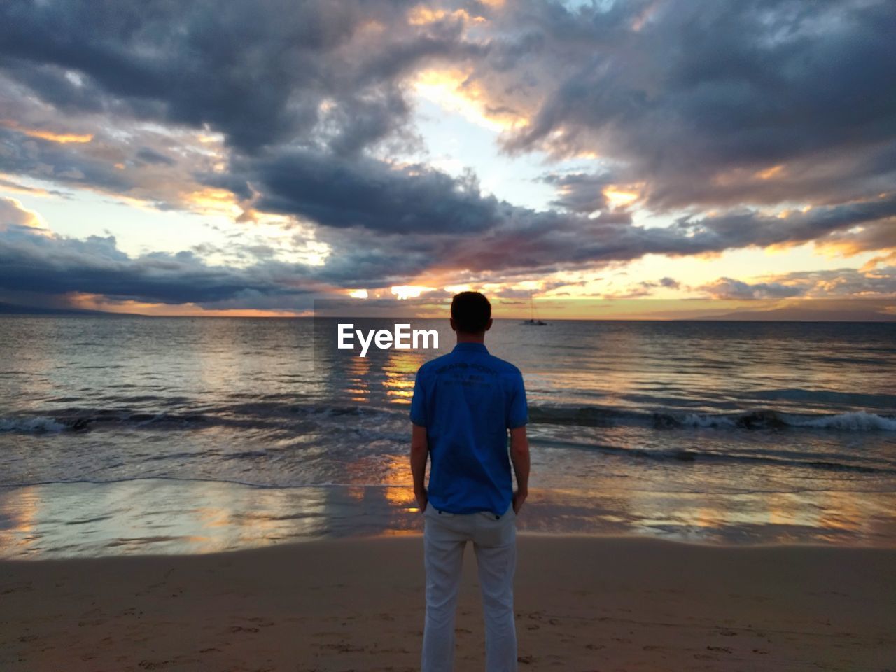 Rear view of man standing at beach against sky during sunset