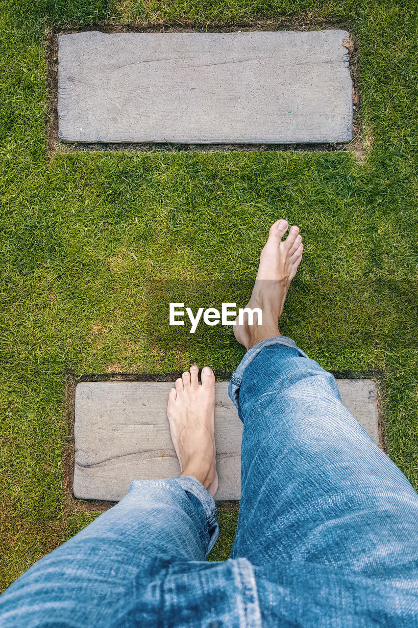 LOW SECTION OF MAN SITTING ON GREEN GRASS