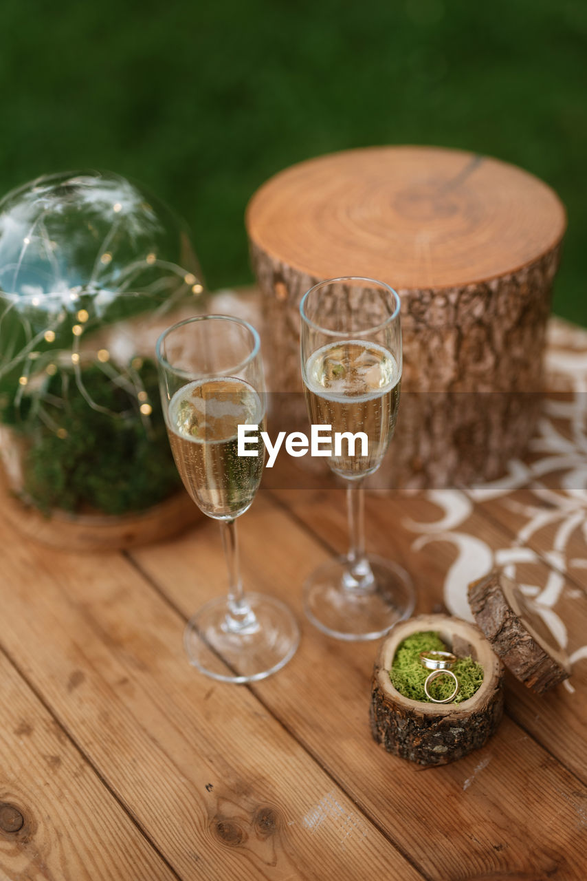 glass, food and drink, wine, alcohol, drink, refreshment, drinking glass, wine glass, wood, table, no people, green, household equipment, food, celebration, champagne flute, nature, stemware, plant, drinkware, focus on foreground, lighting, champagne, alcoholic beverage, outdoors, selective focus, day