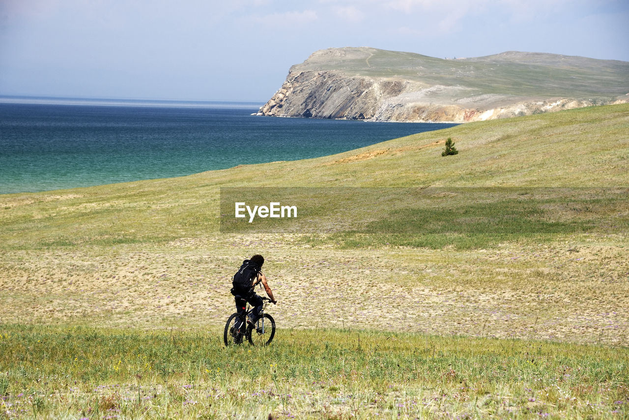 Rear view of man riding bicycle on land against sky