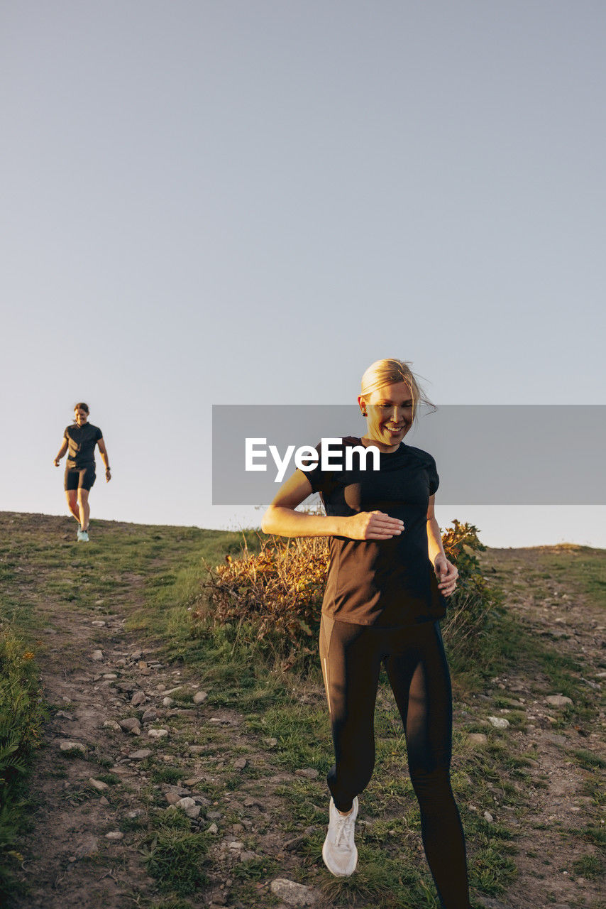 Smiling woman running down from hill against sky