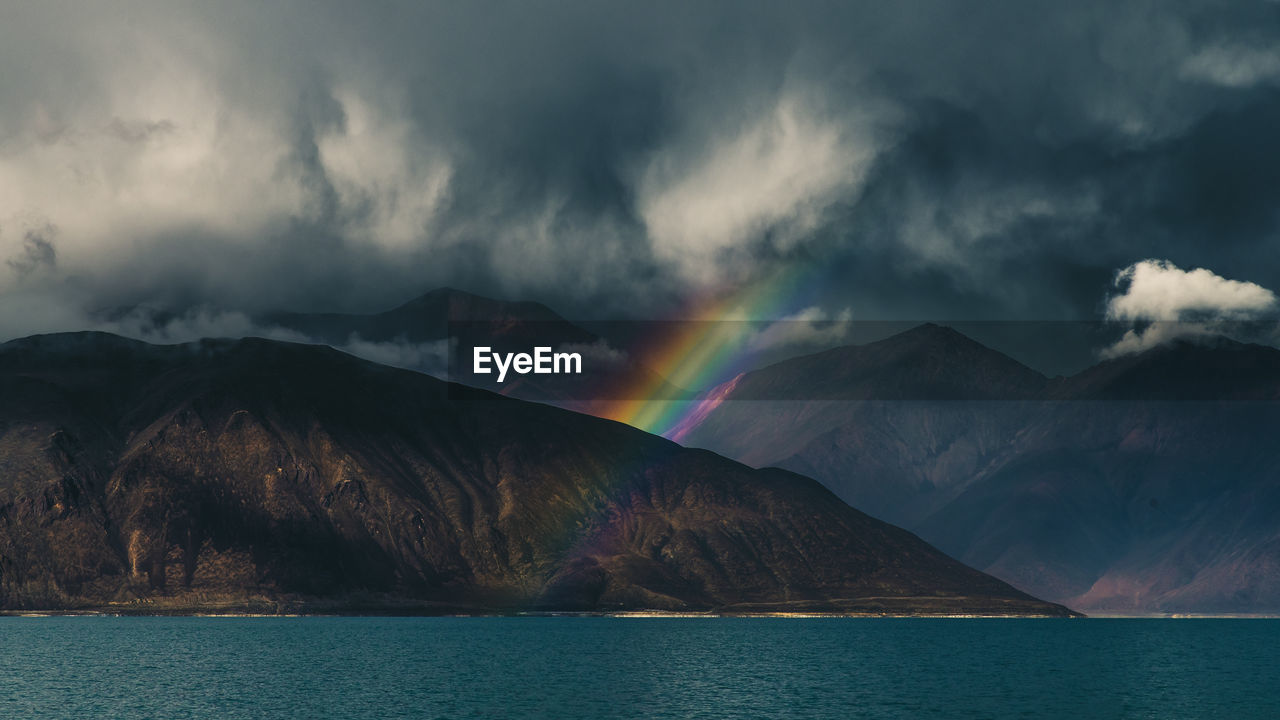 Rainbow over lake and mountains against sky