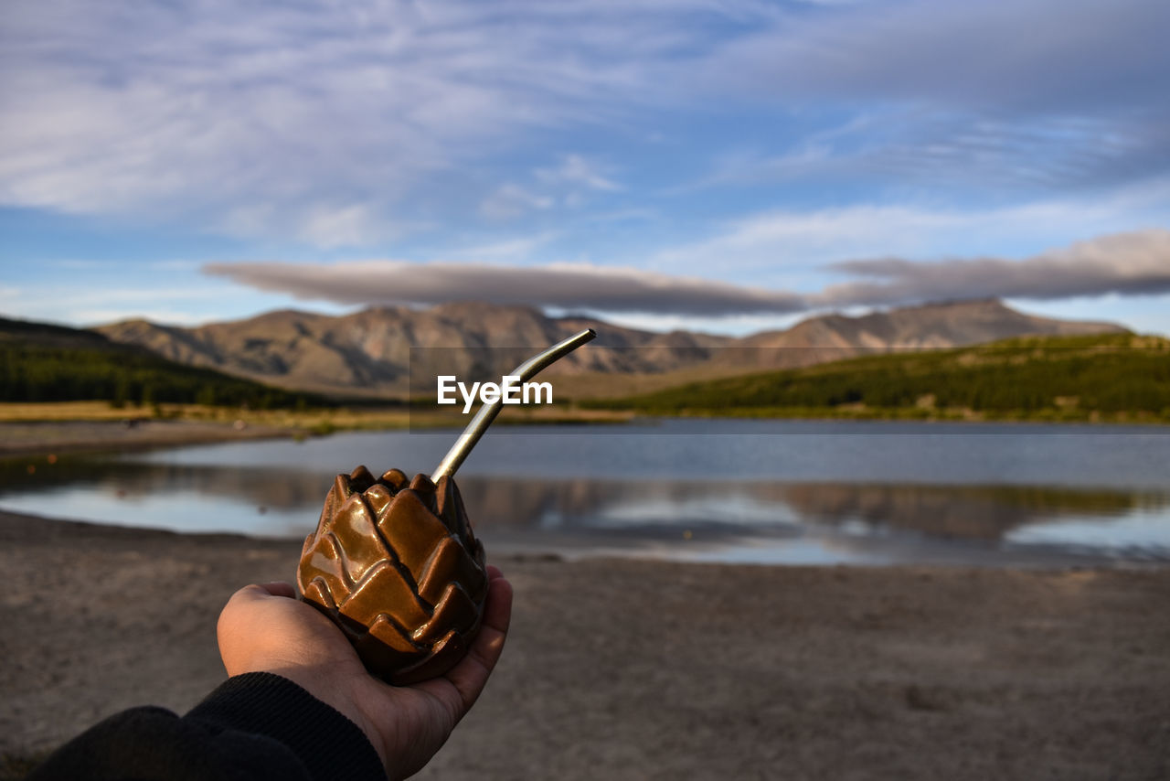 PERSON HOLDING UMBRELLA ON SHORE AGAINST SKY