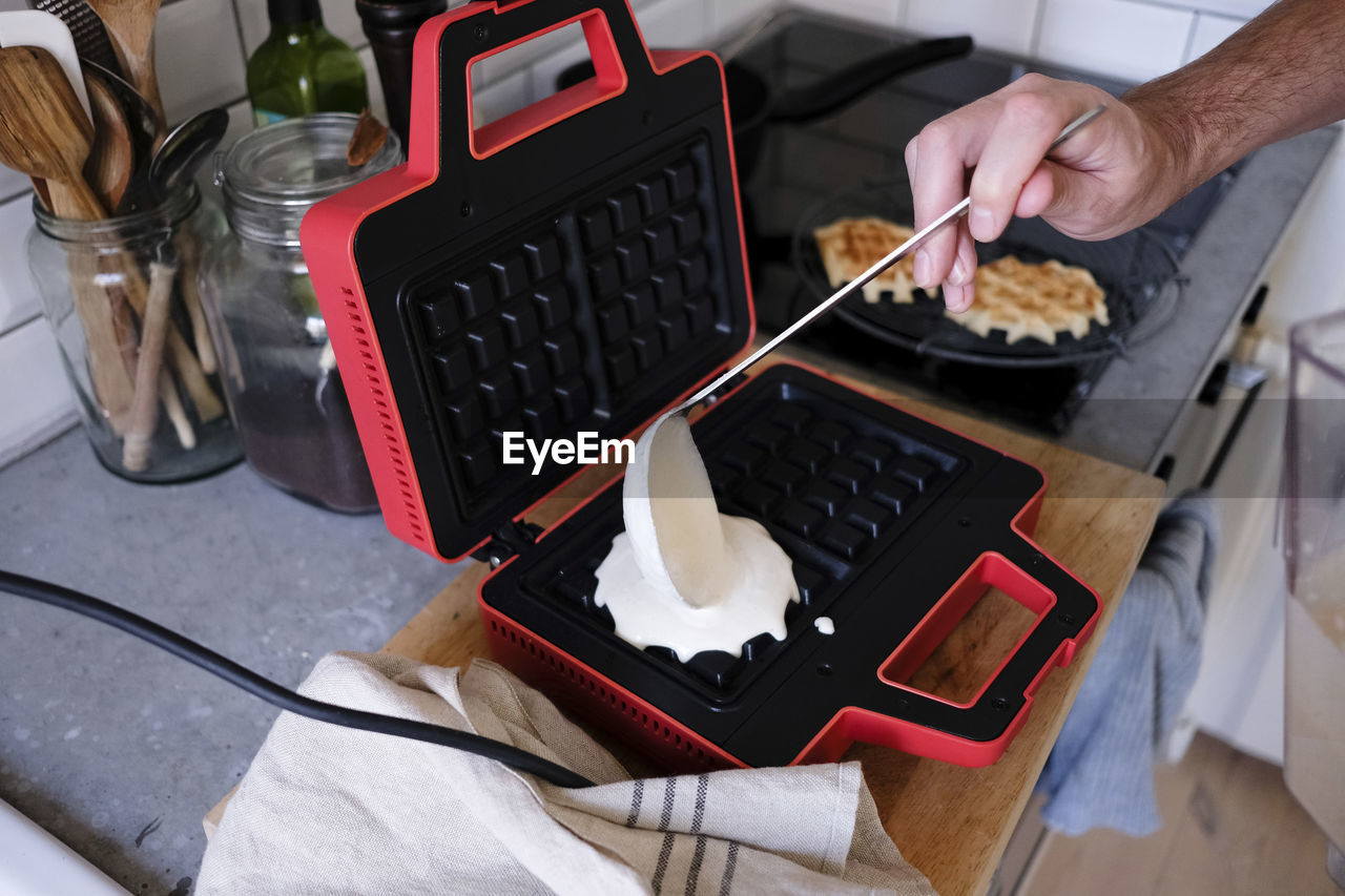 Cropped image of man pouring batter on waffle iron at kitchen counter