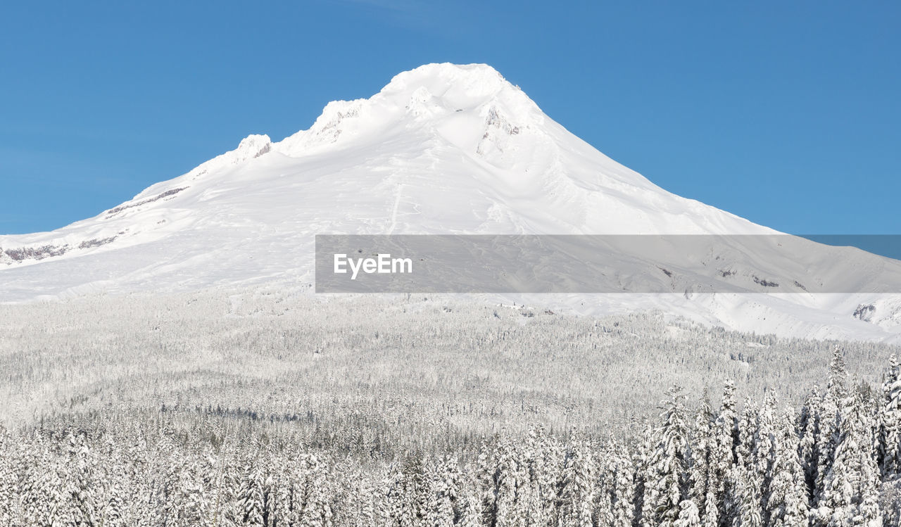 Low angle view of snowcapped mountains against clear blue sky