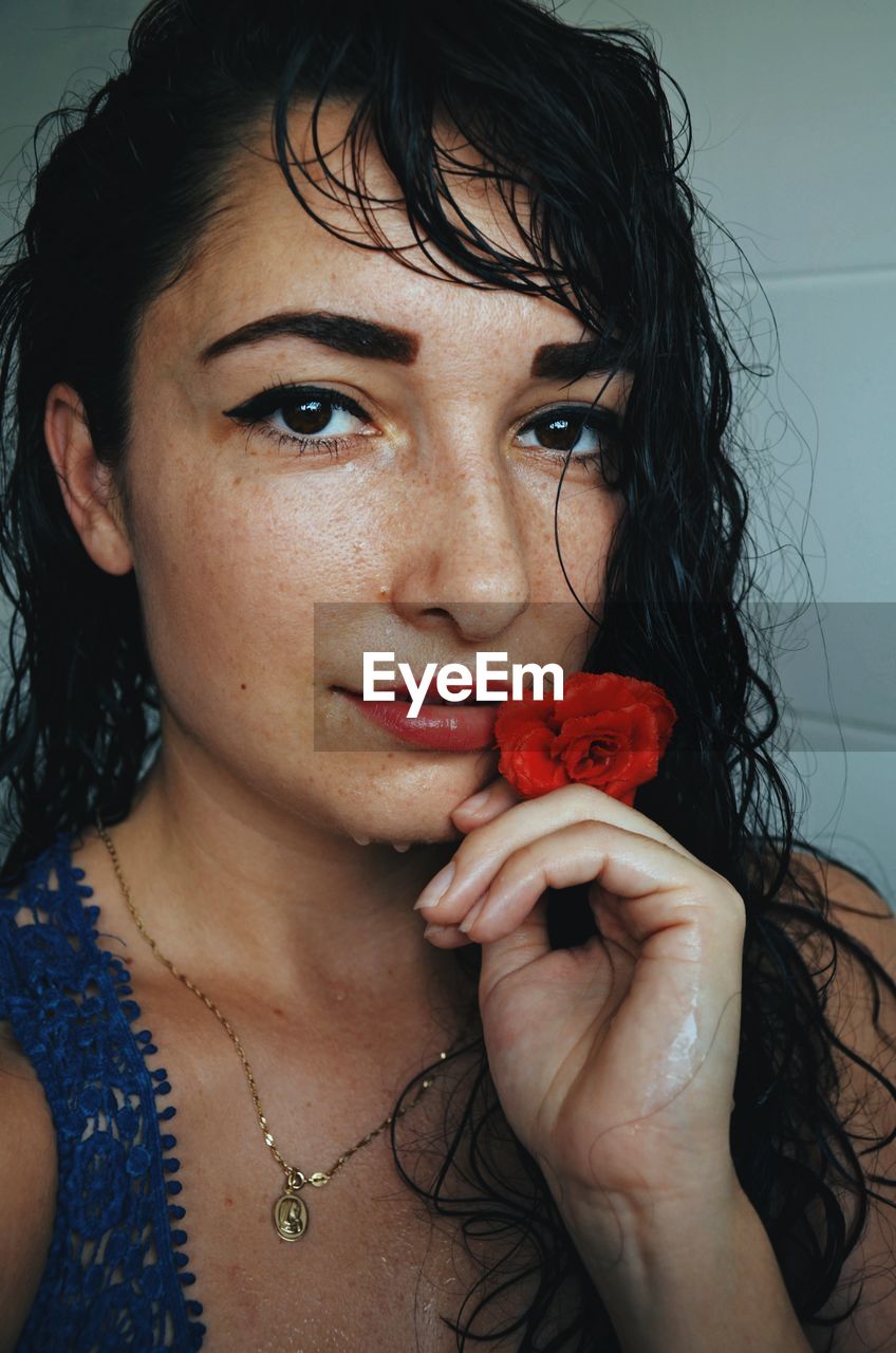 Close-up portrait of woman with red rose at home