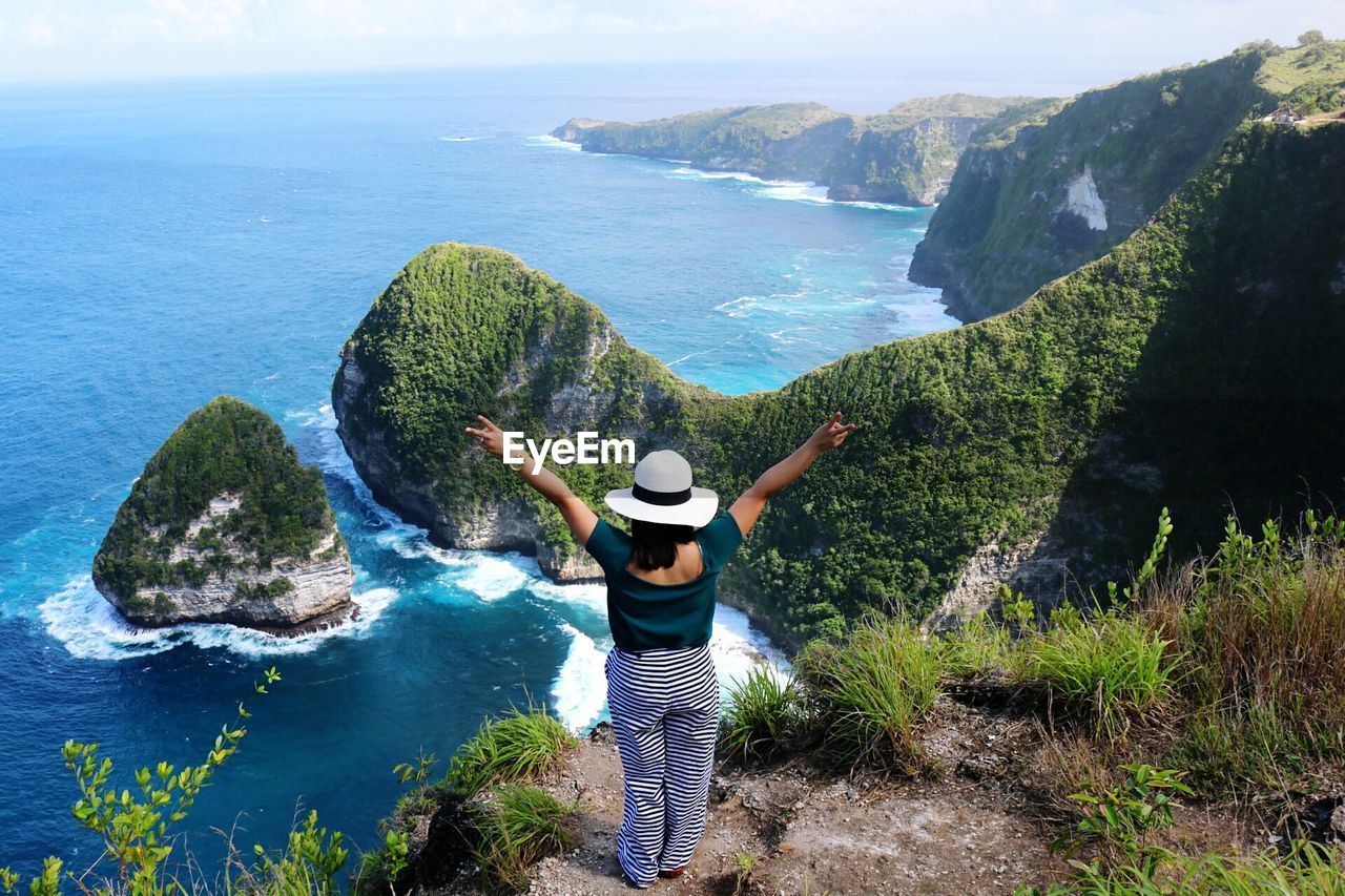 Rear view of woman with arms raised looking at sea while standing on mountain