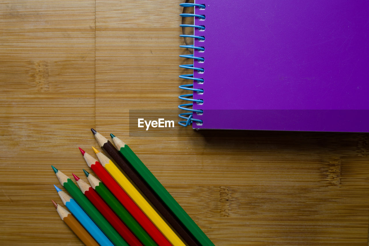 High angle view of colorful pencils with book on wooden table