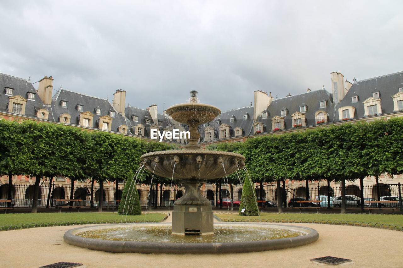 VIEW OF FOUNTAIN IN GARDEN AGAINST CLOUDY SKY