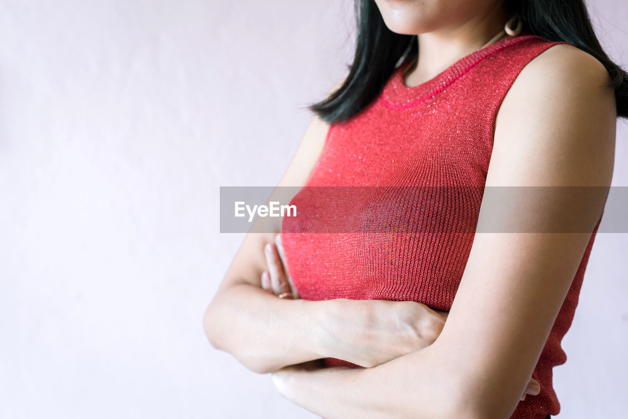 Midsection of woman touching breast while suffering from cancer while standing against white background