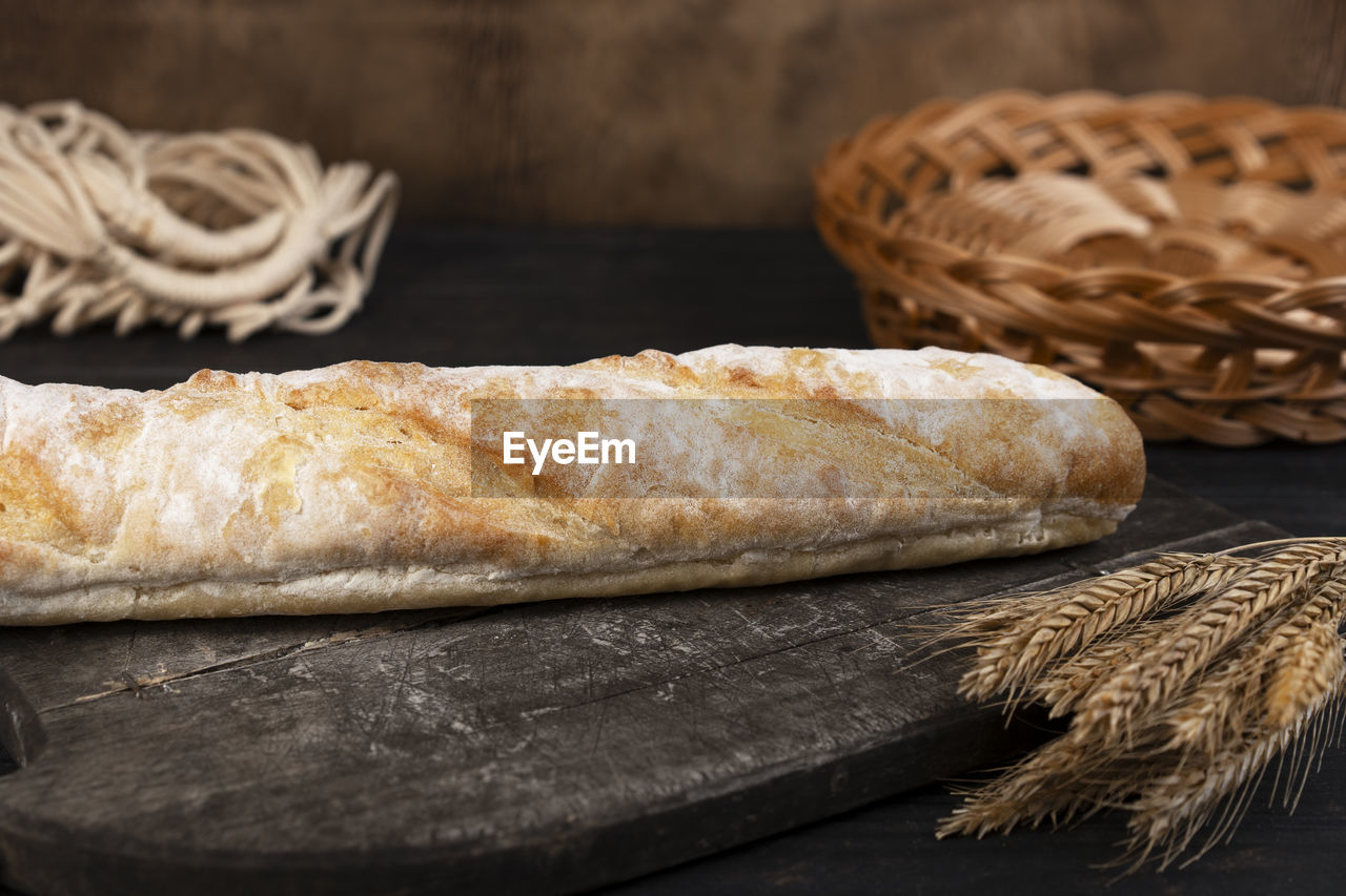 Homemade fresh crispy baguette bread in a cutting board. wooden background. side view.