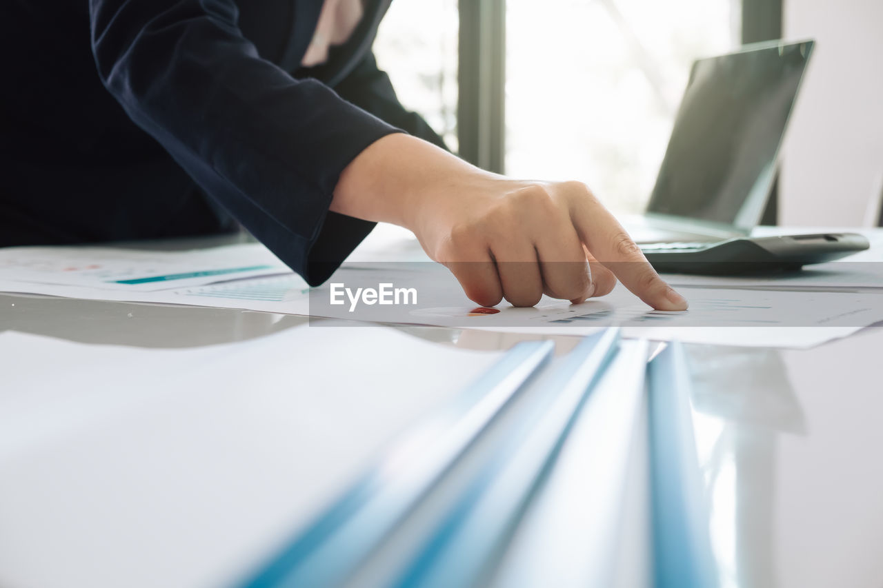 Cropped image of businesswoman analyzing paperwork on table