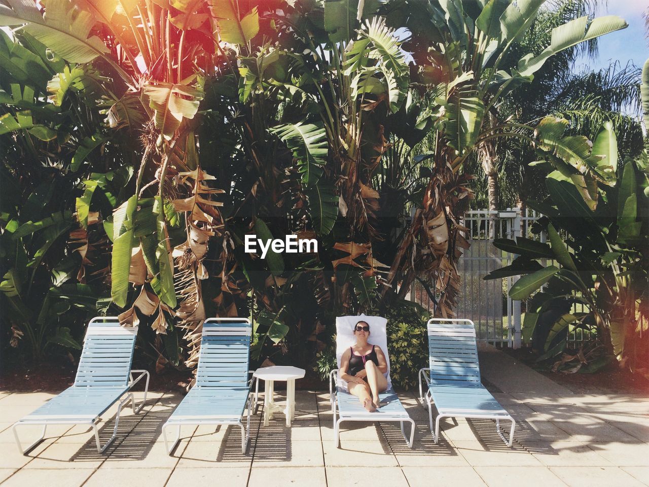 Full length of woman relaxing on lounger chair against trees