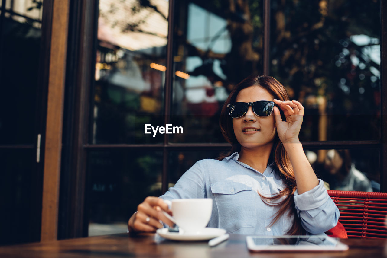 Young woman wearing sunglasses while having coffee at restaurant