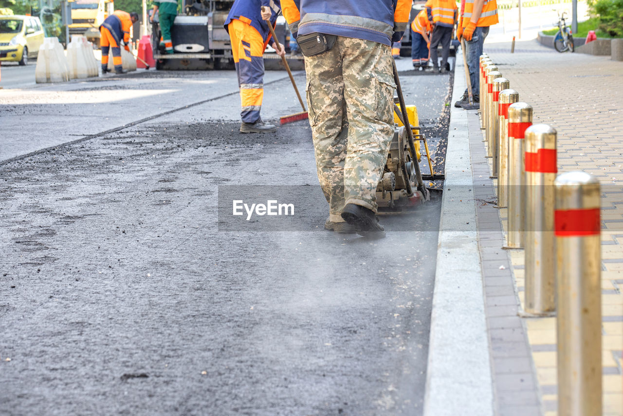 asphalt, road, transportation, occupation, city, street, group of people, men, protection, working, road construction, day, construction industry, walking, adult, security, sign, clothing, reflective clothing, road surface, industry, construction site, architecture, outdoors, manual worker, motion, traffic cone, mode of transportation, construction worker, vehicle, protective workwear, coworker, low section, uniform