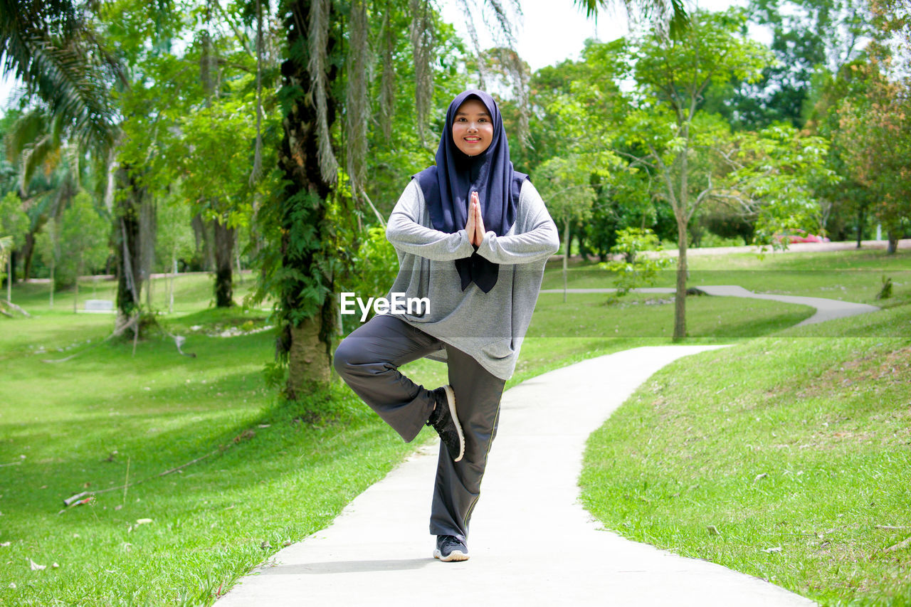 PORTRAIT OF SMILING YOUNG WOMAN AGAINST TREES IN PARK