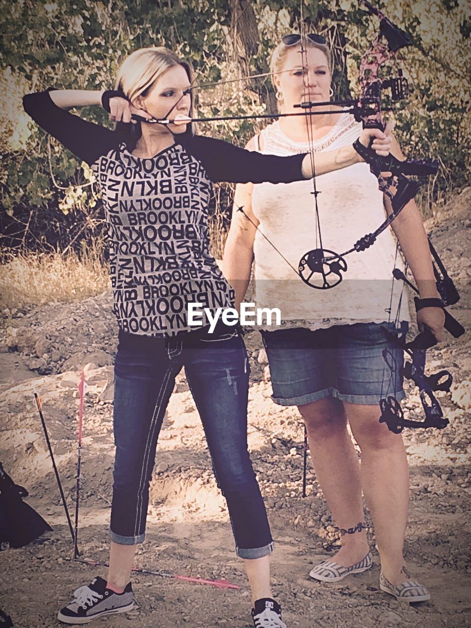 Friend looking at young woman practicing archery against trees at forest