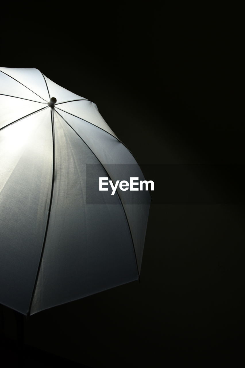 Low angle view of electric light emitting behind umbrella against black background