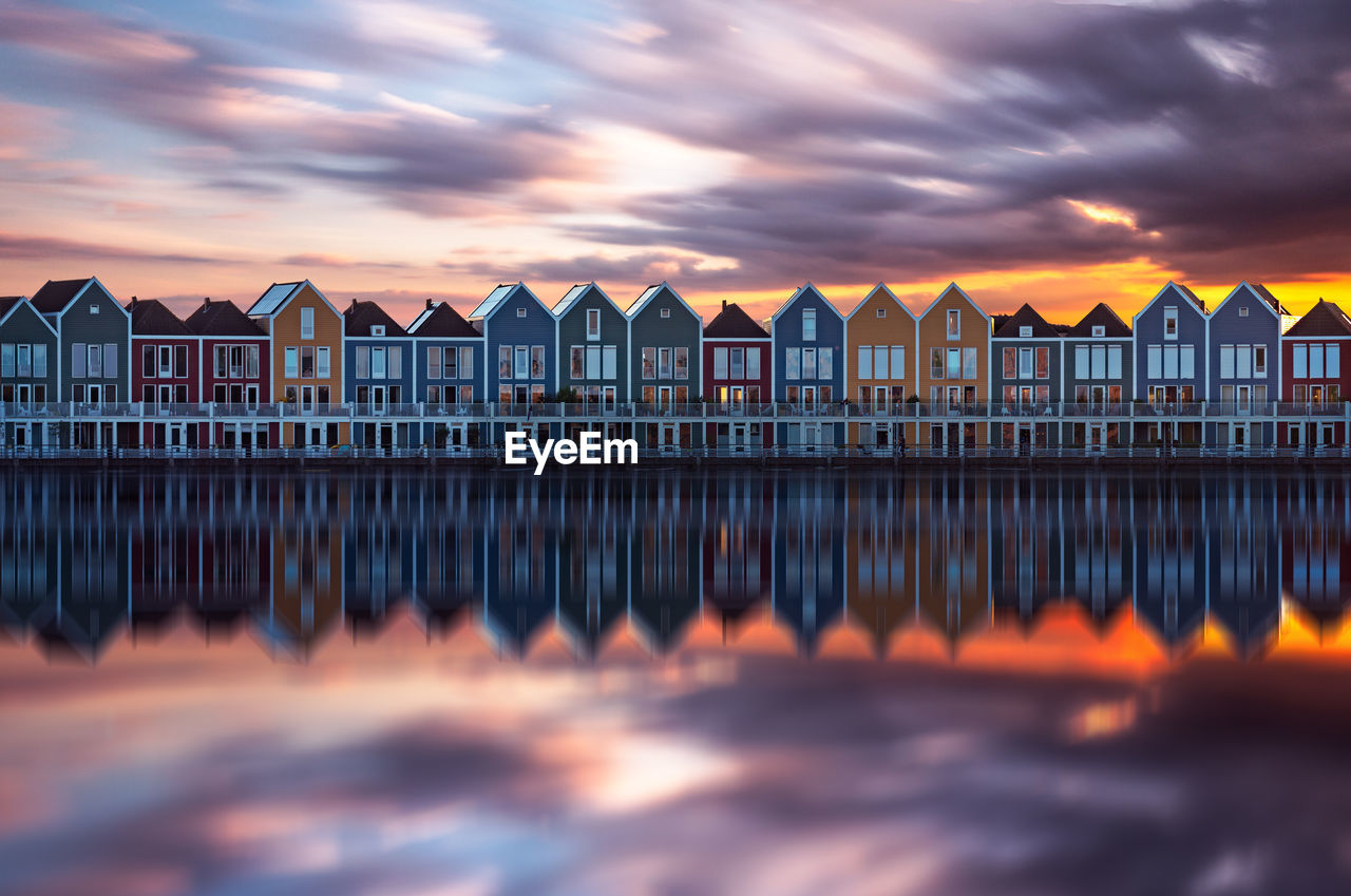Reflection of colorful houses on calm sea against cloudy sky at sunset
