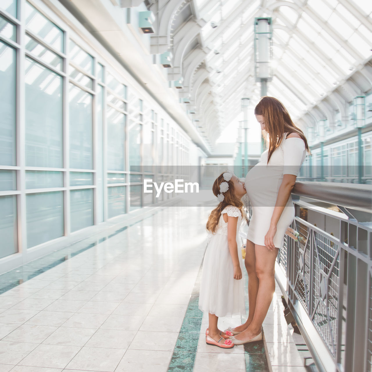 Side view of pregnant mother with daughter standing in corridor