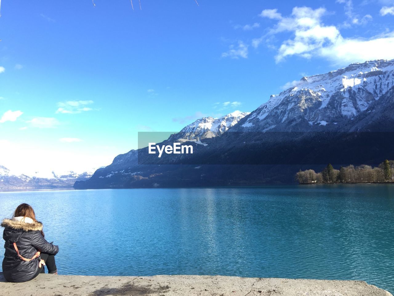 Rear view of woman sitting by lake during winter