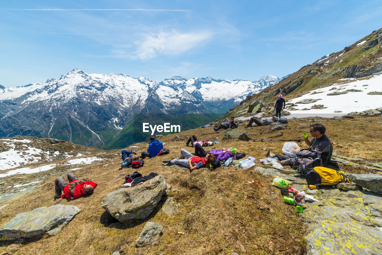 Hikers resting on mountain against sky