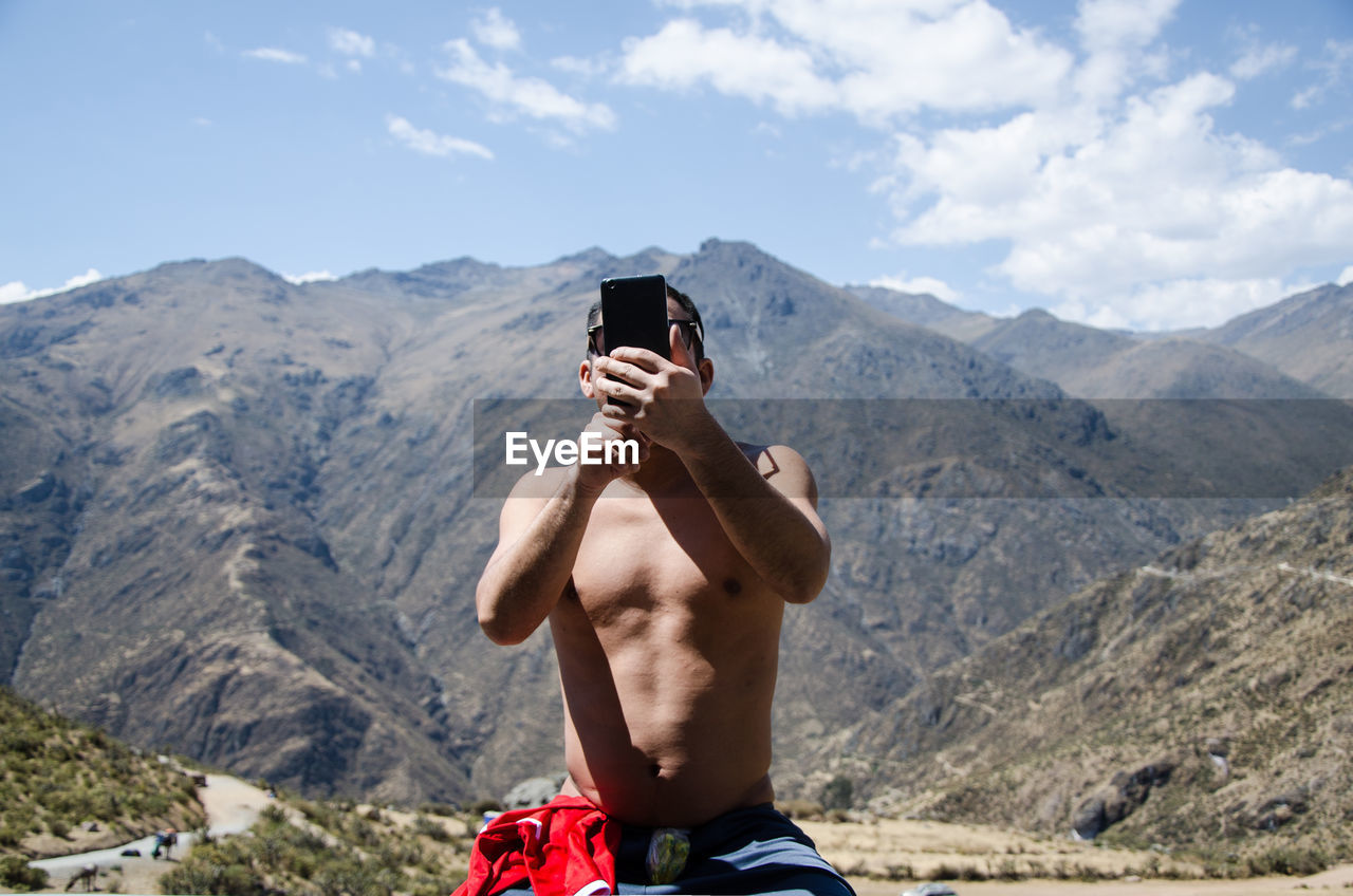 Shirtless man using mobile phone against mountains and sky
