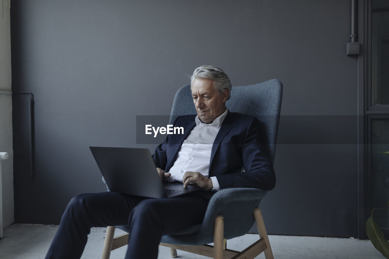 Senior businessman sitting in armchair using laptop