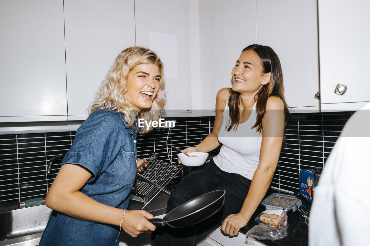 Happy multiracial female friends laughing in dorm room kitchen