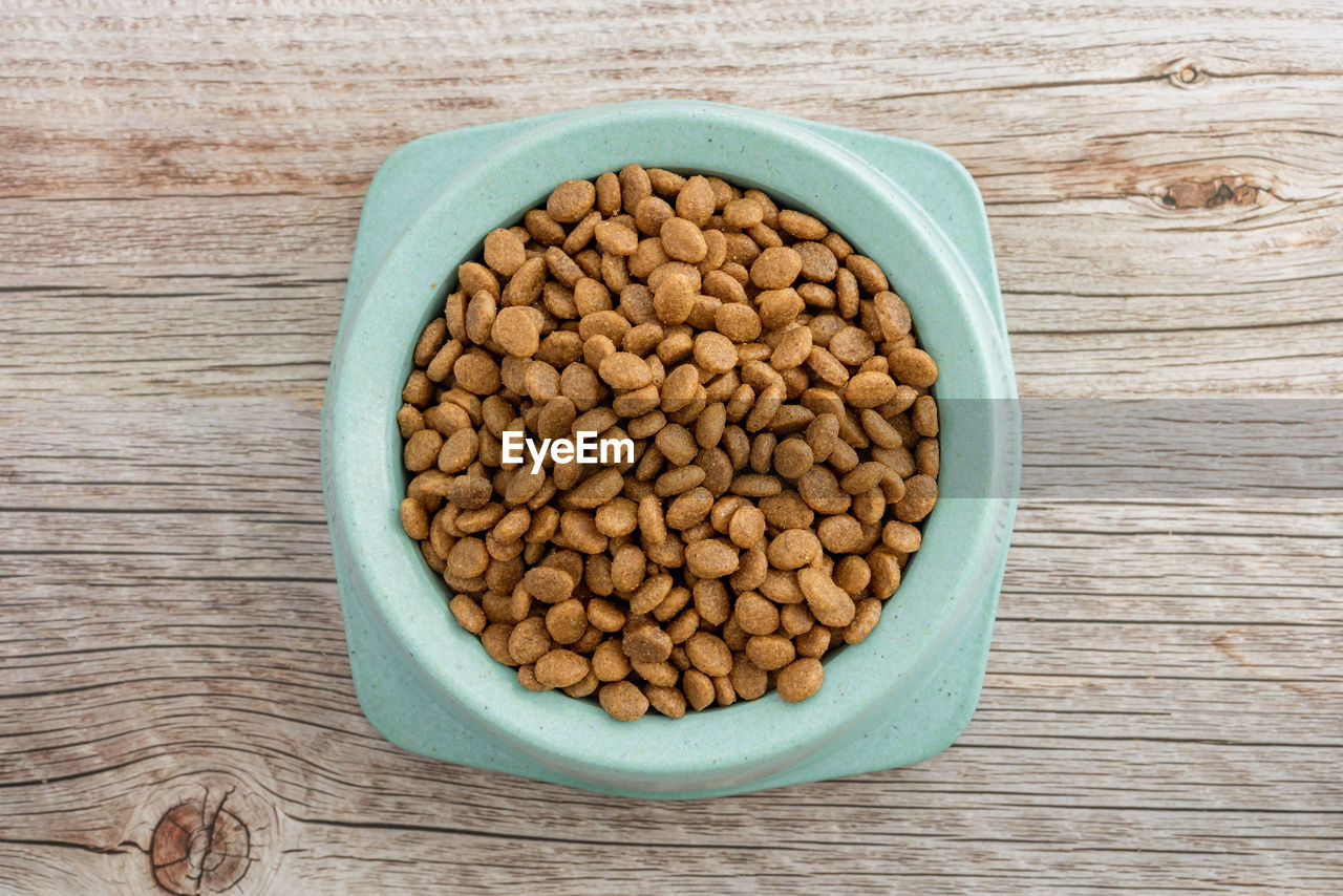 Dry food for cats and dogs in a green bowl on a wooden background. top viev.