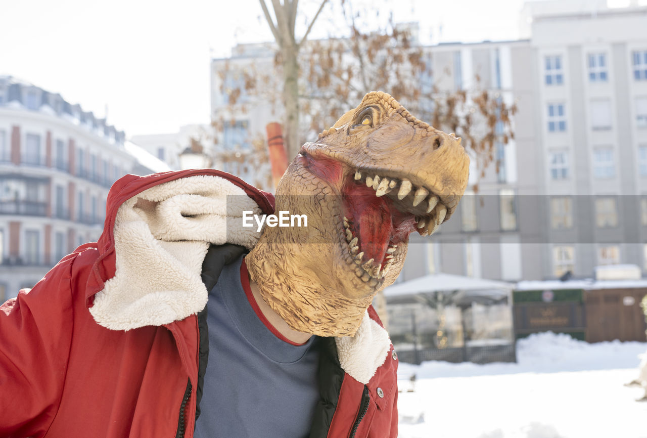 Man wearing dinosaur mask standing in city