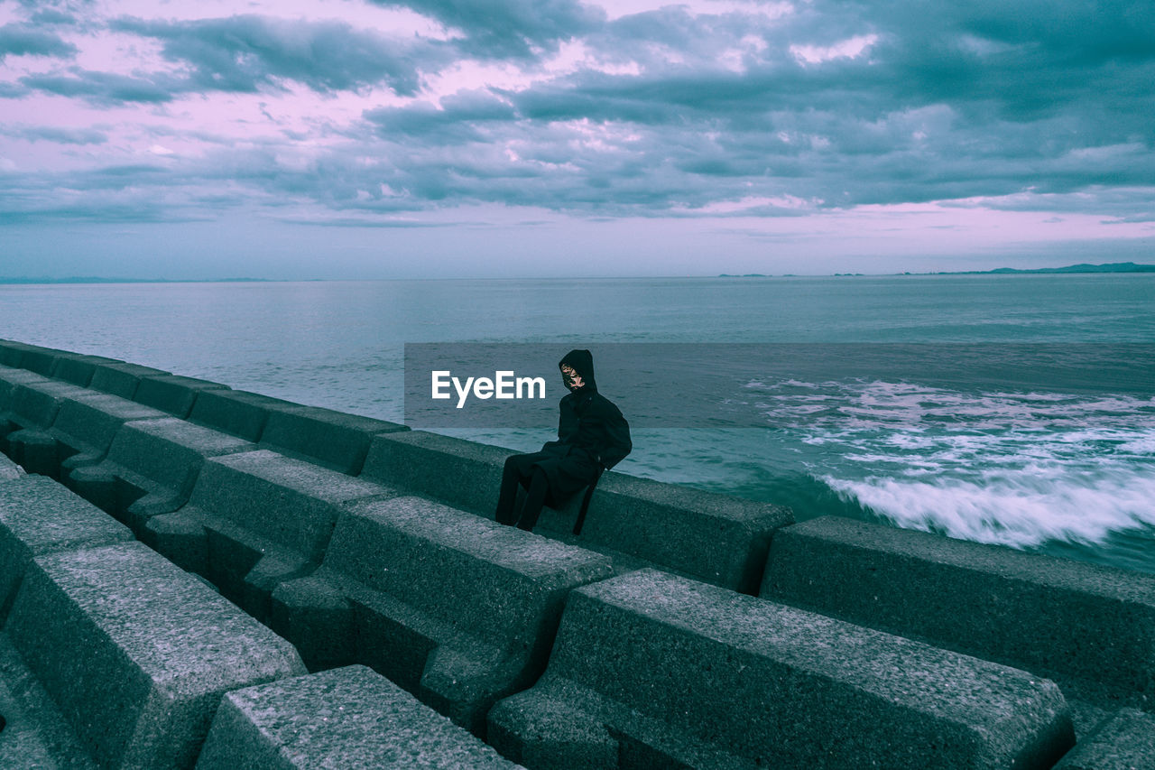 Man wearing mask while sitting against sea and sky