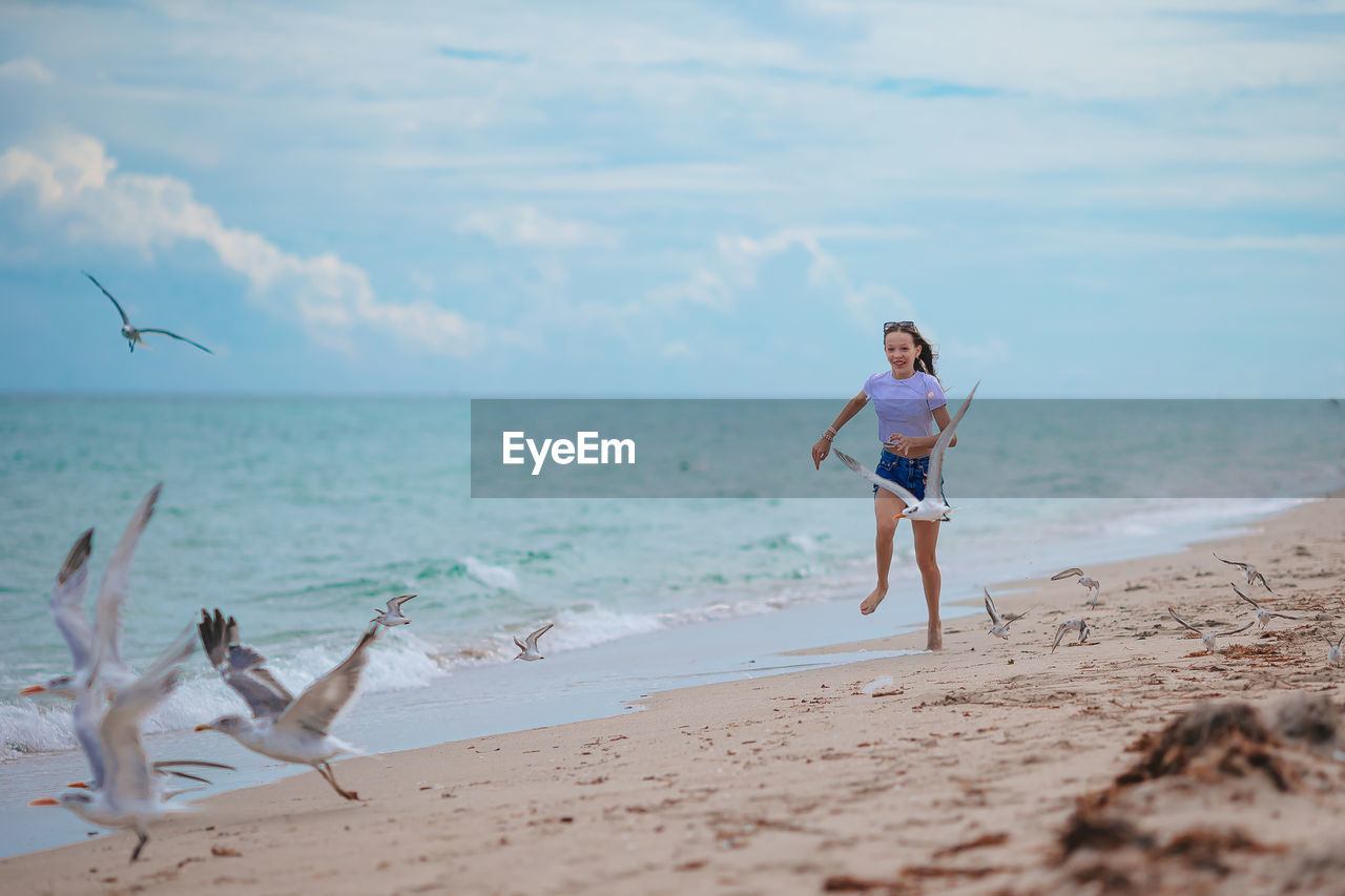 full length of young woman standing at beach against sky