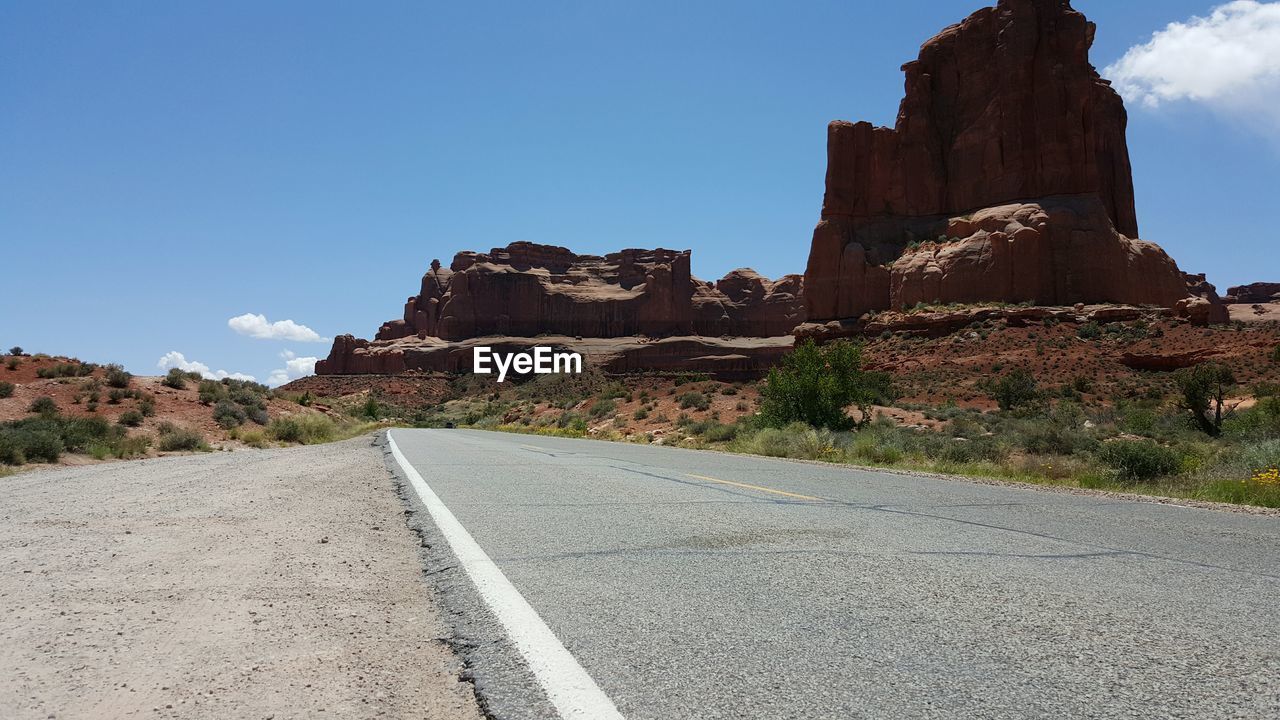 Road leading towards mountain against blue sky