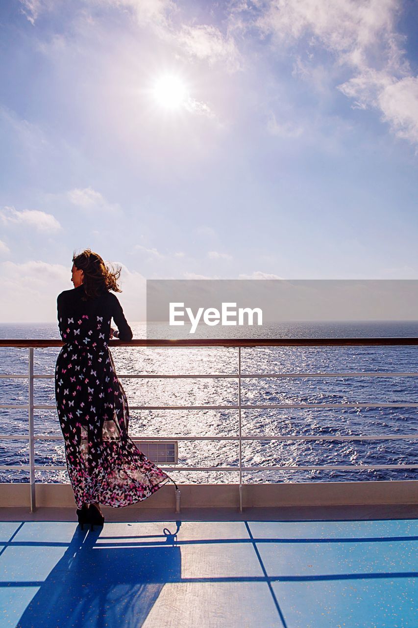 Rear view of woman standing by railing on boat deck in sea against sky