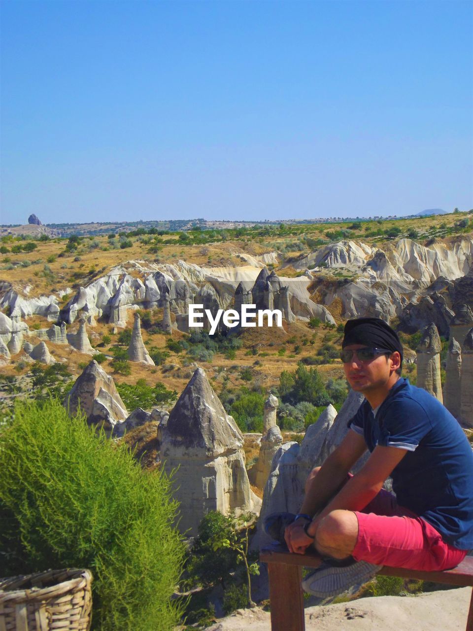Man looking away while sitting on rocks at nevsehir against clear blue sky