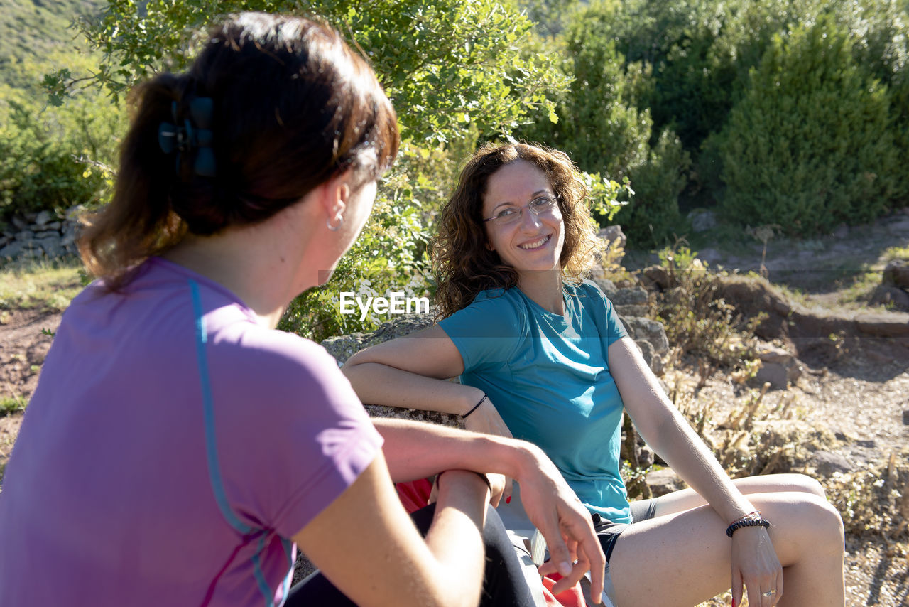 Two hiker girls resting and chating on a mountain path side.