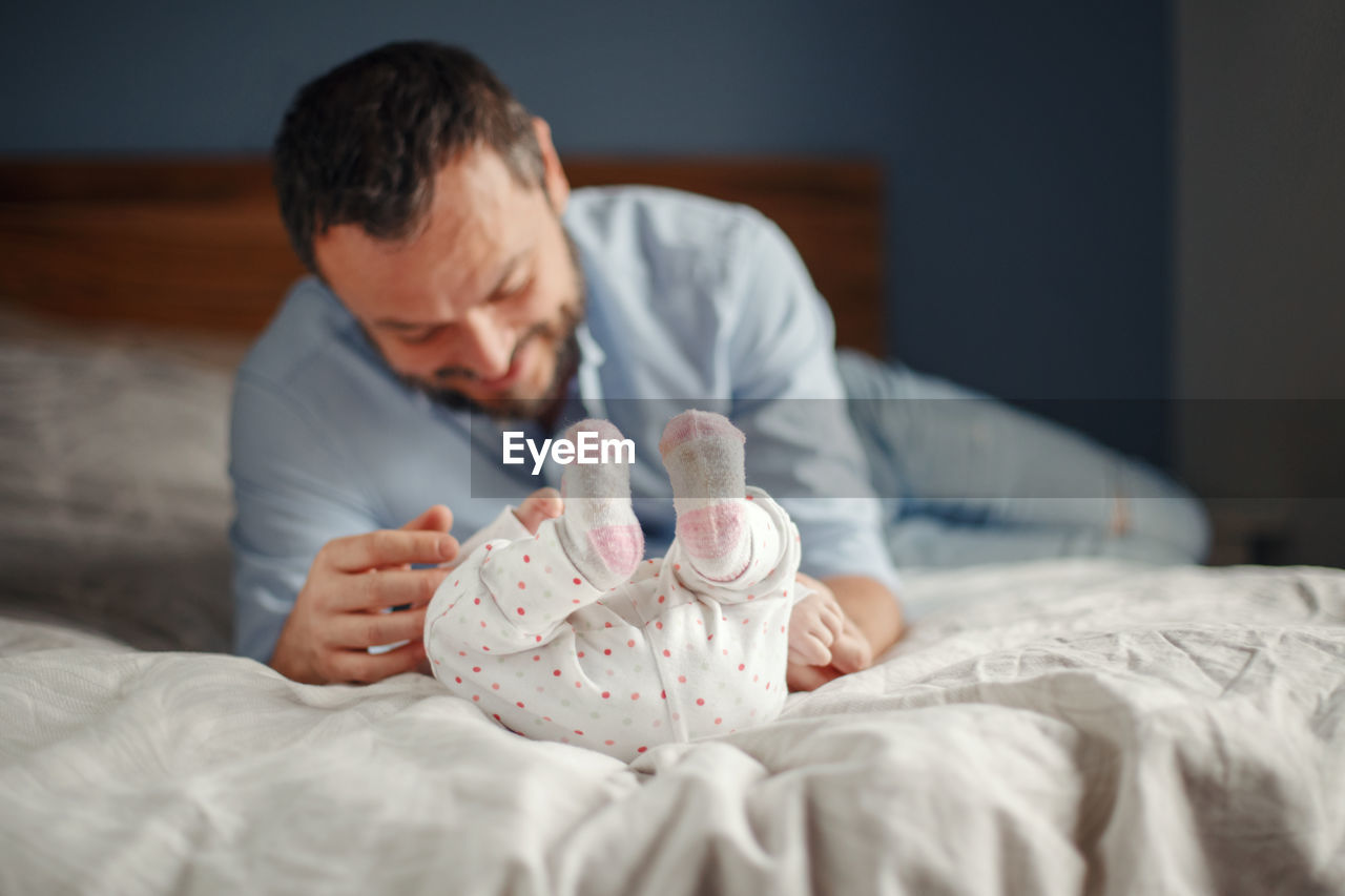 Father playing with daughter while lying on bed at home