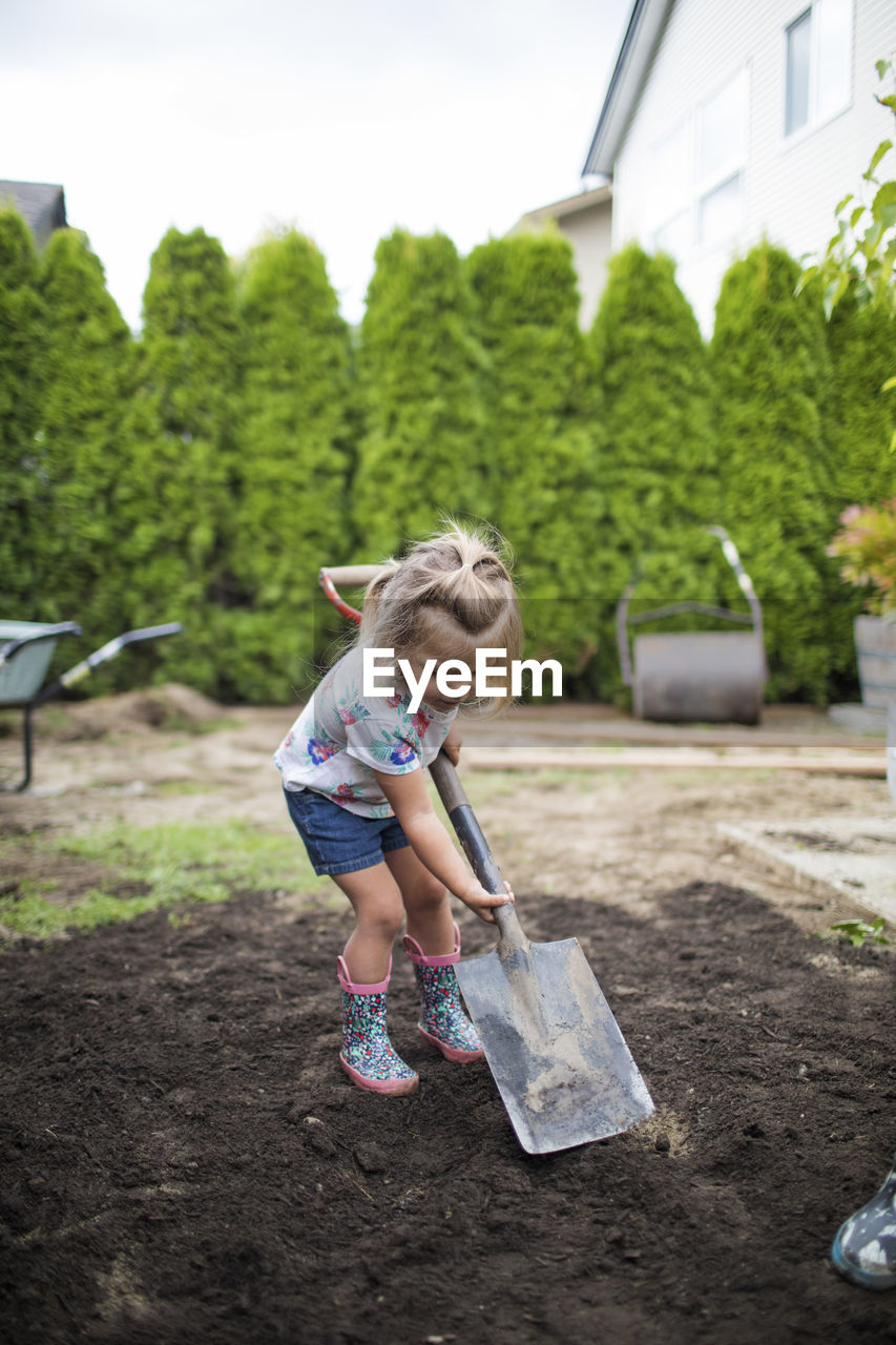 Two year old girl shoveling dirt in her backyard.