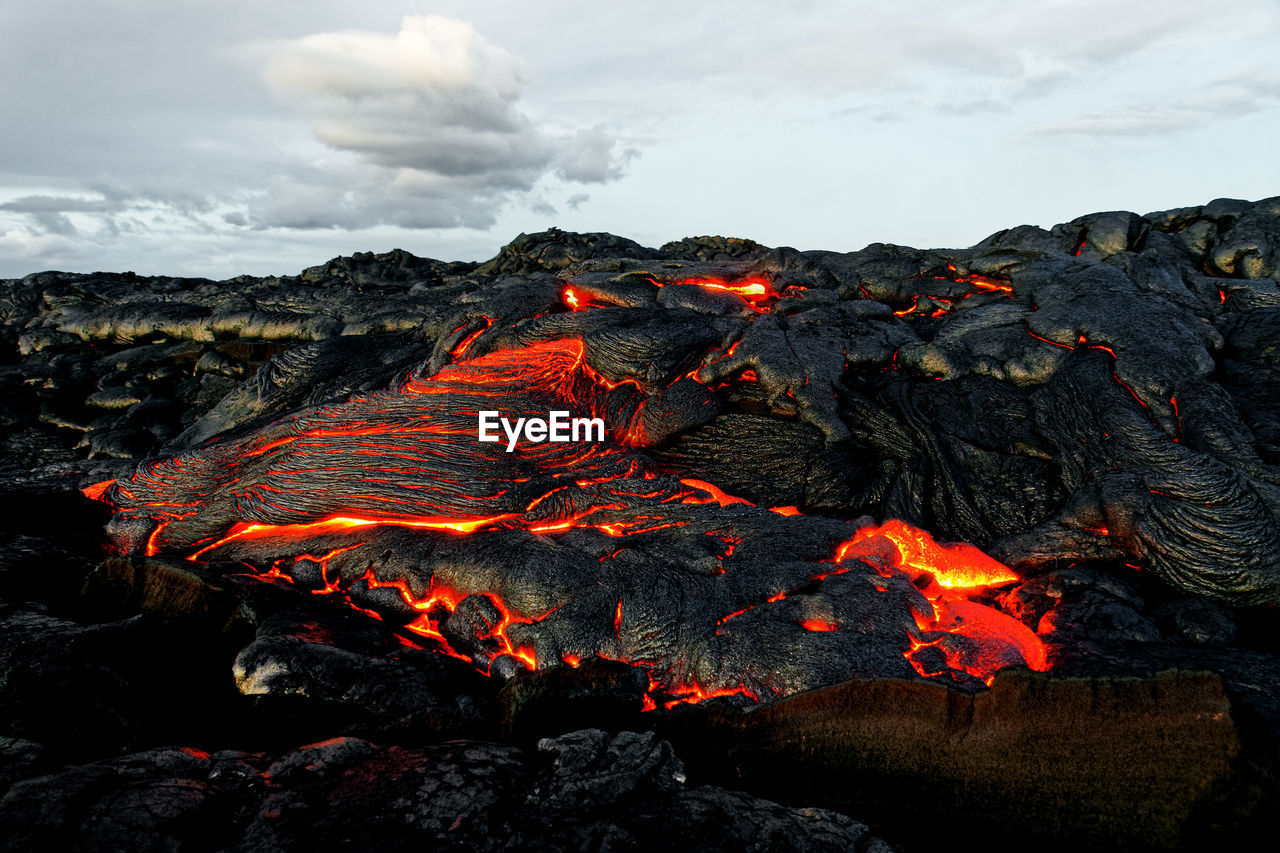 A lava flow emerges from a rock column and pours into a black volcanic landscape, hawaii, big island