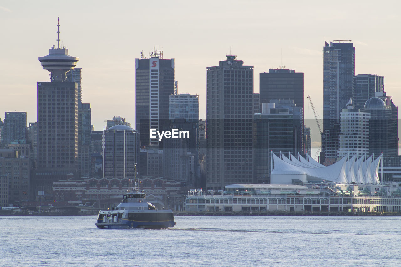 Ferry boat sailing in river against buildings in city
