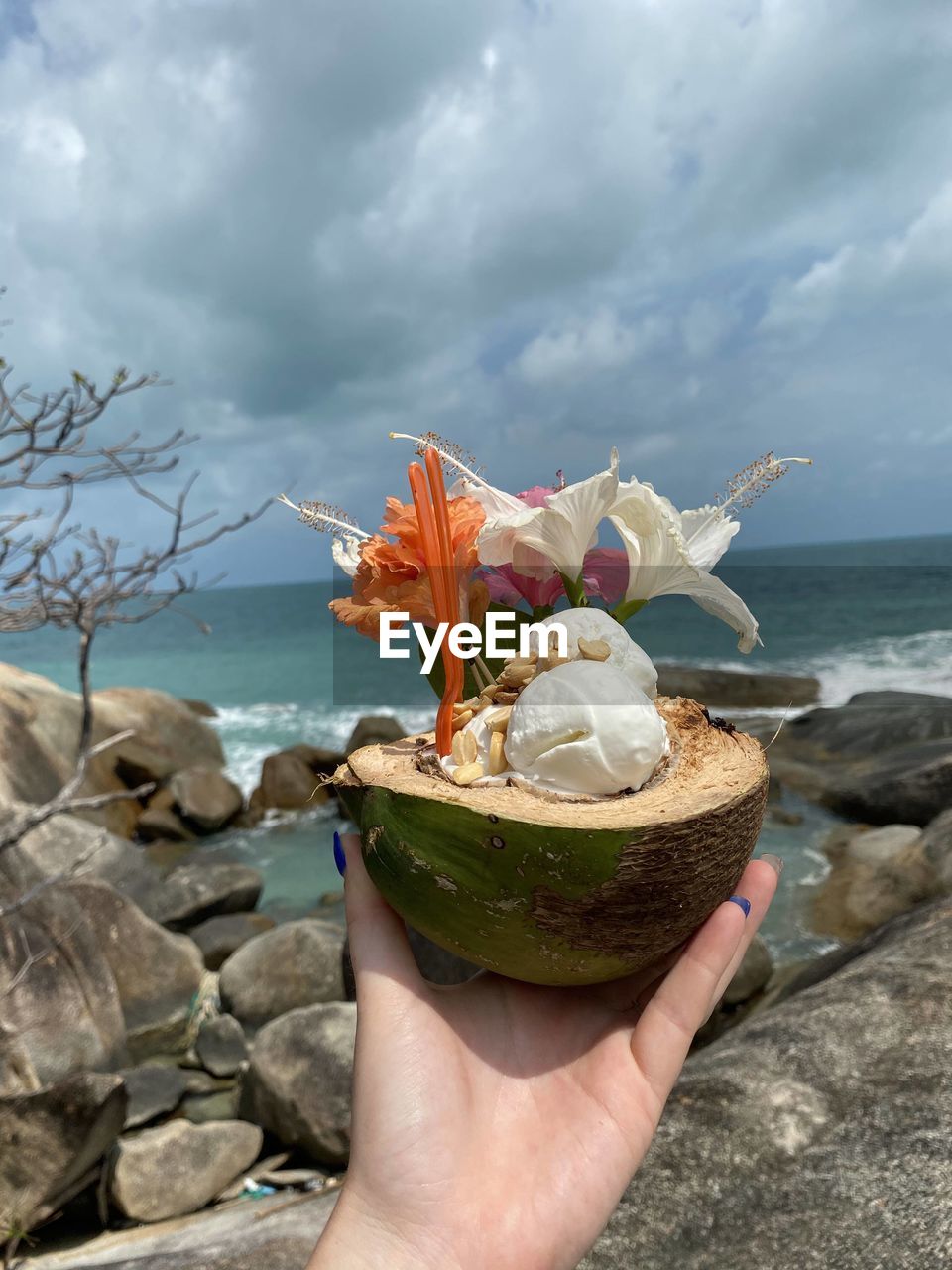 Cropped hand of woman holding coconut while standing against sea